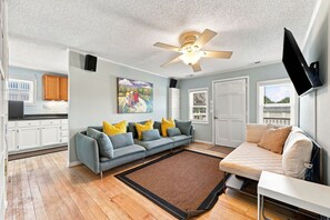 Ein Wohnzimmer mit Sofa, Couchtisch, Wandfernseher und Deckenventilator.
