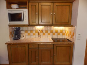 A compact kitchen with wooden cabinets, a microwave, a coffee maker, and a tiled backsplash. - 3-star duplex - 4 guests (Pralognan-la-Vanoise)