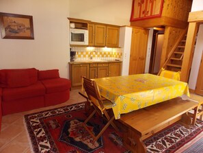 Ein kompakter Wohnbereich mit einer Küche, einem Esstisch mit gelber Tischdecke, einem roten Sofa und einer Treppe, die zu einer oberen Ebene führt.