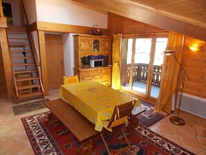 A cozy room with a wooden table, a bench, a ladder, a microwave, and a sliding glass door leading to an outdoor area. - 3-star duplex - 4 guests (Pralognan-la-Vanoise)