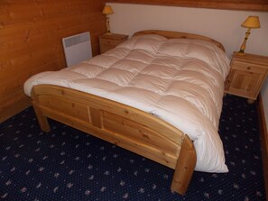 A wooden bed with a white duvet in a room with wooden walls and a dark patterned carpet. - 3-star duplex - 4 guests (Pralognan-la-Vanoise)