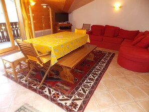 A dining area with a wooden table and chairs, a red sofa, and a patterned rug. - 3-star duplex - 4 guests (Pralognan-la-Vanoise)