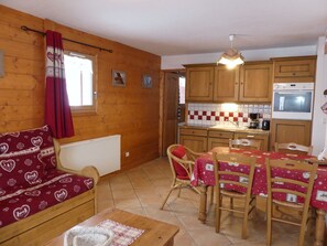 A cozy room with a sofa, a dining table with chairs, a kitchen area with wooden cabinets, and a window with curtains. - Convenient apartment - 6 guests (Pralognan-la-Vanoise)