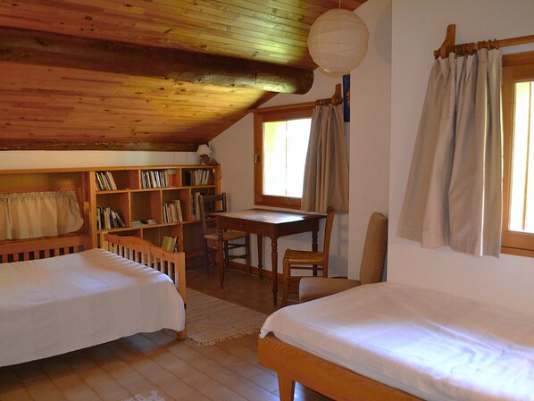 A cozy room with two beds, a wooden desk, a bookshelf, and a window with curtains.