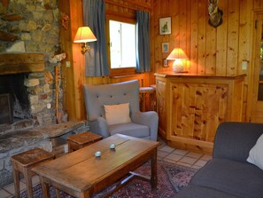 A cozy room with a stone fireplace, a wooden table, a grey sofa, and a wooden cabinet with a lamp on top.