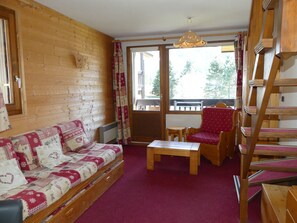 Ein gemütliches Zimmer mit einer Holzwand, einem Sofa, einem Tisch, einem Stuhl und einer Holztreppe.