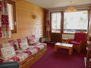 A cozy room with a wooden wall, a sofa with patterned cushions, a wooden table, and a chair with a red cushion. - Cozy duplex near slopes - 6 guests (Pralognan-la-Vanoise)