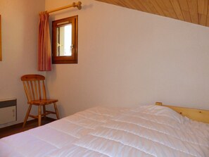 Ein Schlafzimmer mit einem Bett, einem Holzstuhl, einem Fenster mit Vorhängen und einer Heizung.