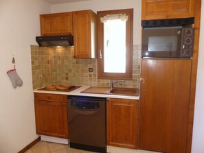 A compact kitchen with wooden cabinets, a built-in oven, a dishwasher, and a window above the sink. - Cozy duplex near slopes - 6 guests (Pralognan-la-Vanoise)