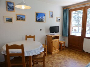 Ett rum med ett matbord, stolar, en tv på ett träställ och inramade tavlor på väggen.