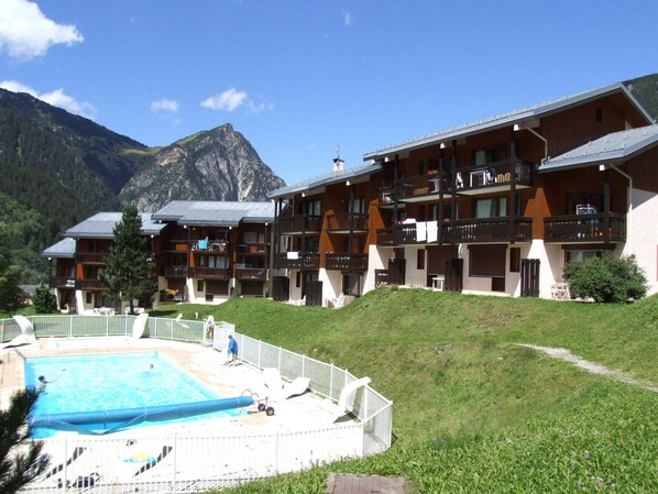Un hotel amb diversos balcons, una piscina i un paisatge de muntanyes al fons.