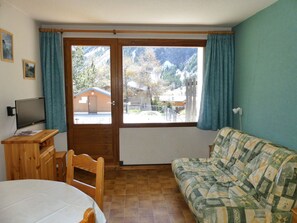 A room with a wooden desk, a television, a sofa, and a view of mountains through a sliding door. - Apartment in Pralognan-la-Vanoise - 5 guests (Pralognan-la-Vanoise)