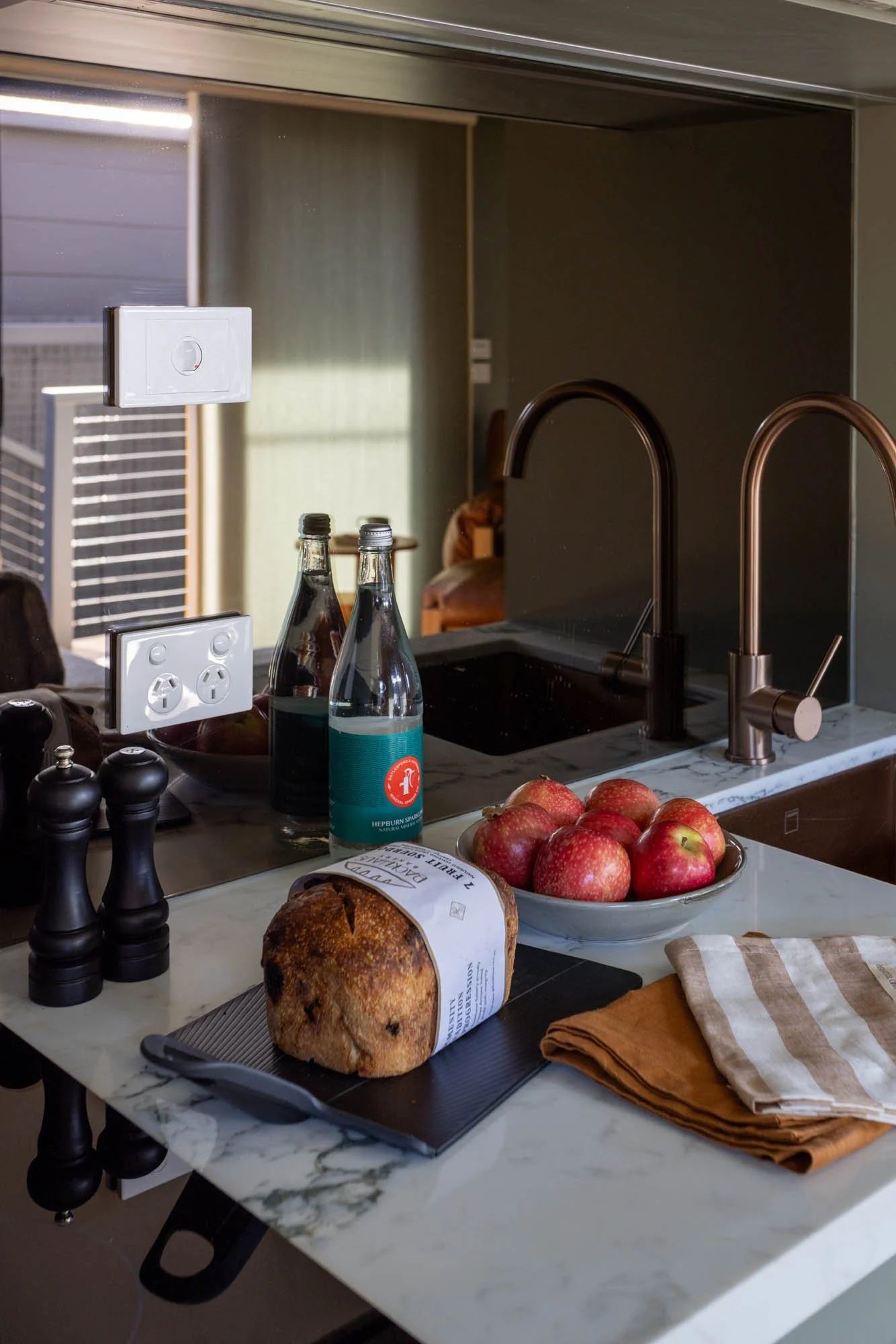 A kitchen counter with a loaf of bread, a bottle of water, and a bowl of apples.
