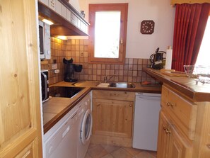 A compact kitchen with wooden cabinets, a washing machine, a coffee maker, and a clock on the wall. - Spacious south-facing apartment - 6 guests (Pralognan-la-Vanoise)