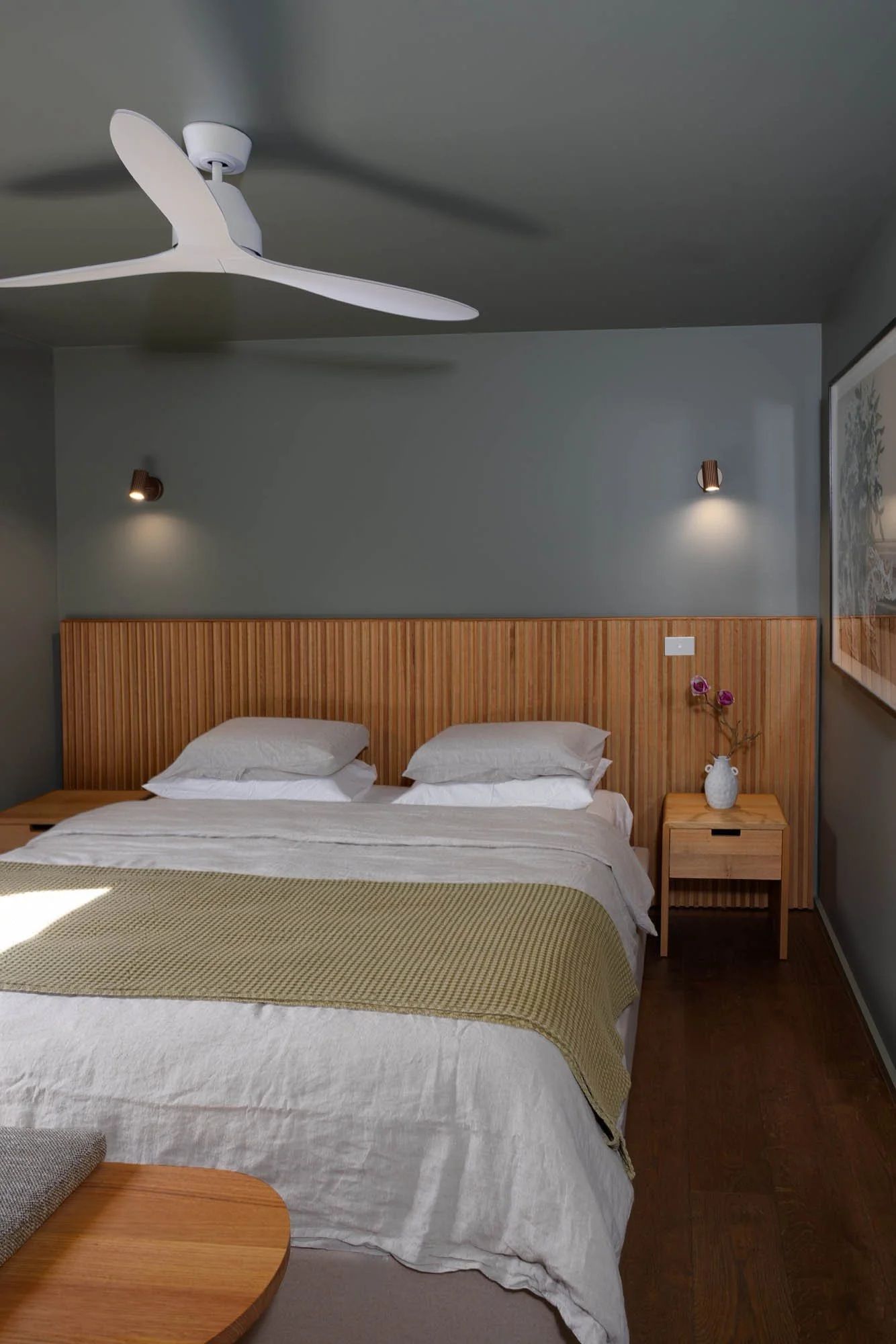 A bedroom with a bed, bedside tables, a nightstand, a ceiling fan, and a wall-mounted light fixture.