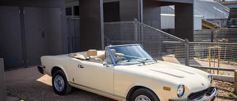 A beige convertible car parked in front of a modern building with a metal fence and a staircase.