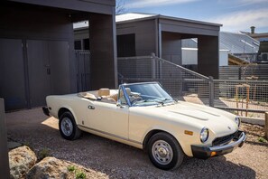 Un'auto decappottabile beige parcheggiata di fronte a un edificio moderno con una recinzione in metallo e una scalinata.