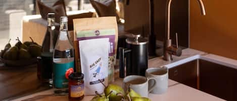 A kitchen counter with a bowl of pears, a bottle of liquor, a jar of jam, a coffee maker, and a bag of coffee.