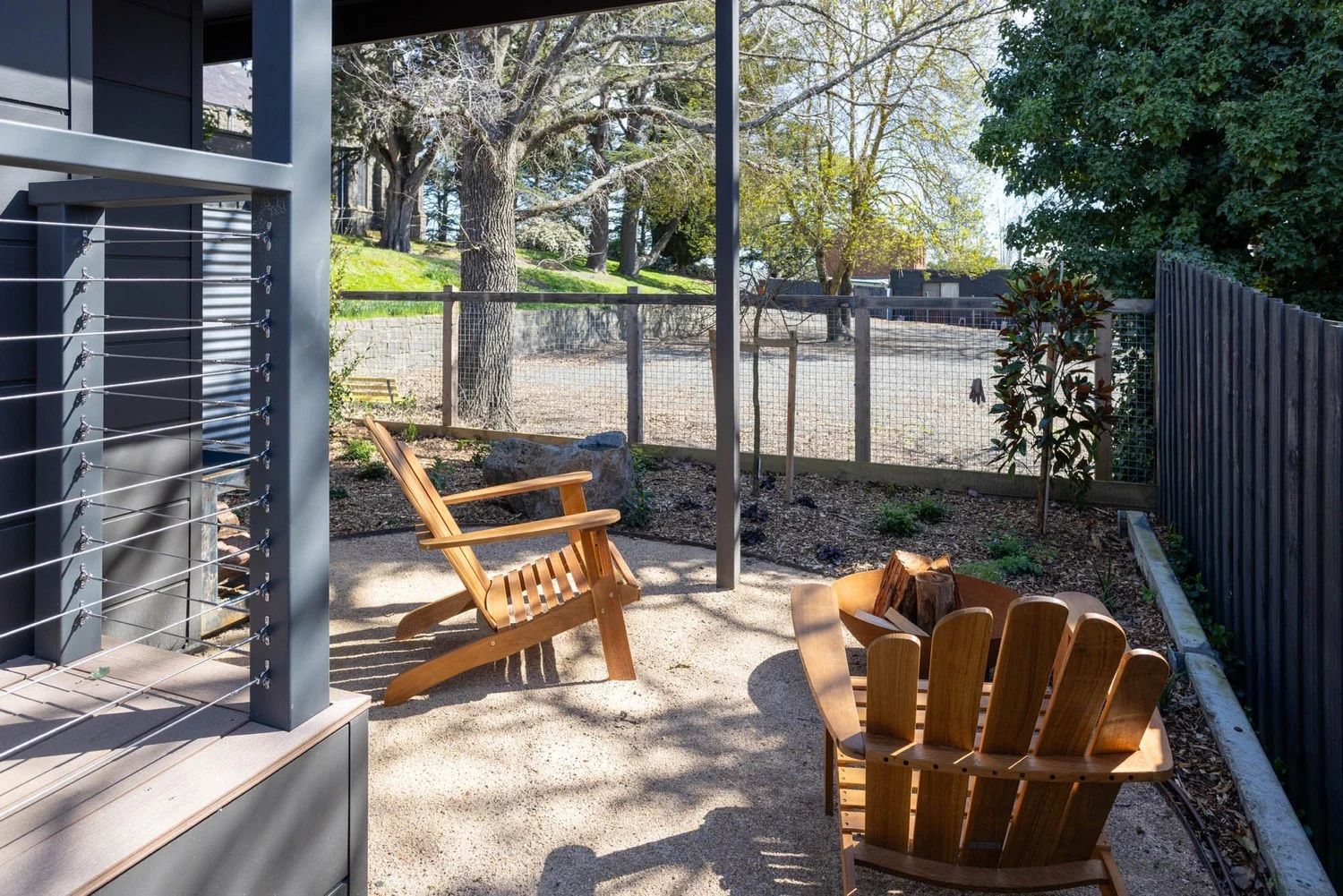 A covered outdoor seating area with two wooden Adirondack chairs and a small round table.