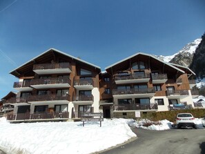 A multi-story hotel with balconies, a sign indicating 'les Hameaux de la Vanoise,' and a snow-covered ground. - Mezzanine studio, pets allowed - 5 guests. Mountain view (Pralognan-la-Vanoise)