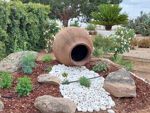 A garden with a large clay pot, rocks, and various plants.