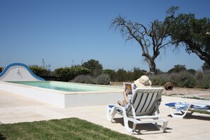 A pool area with lounge chairs and a person reading a book.