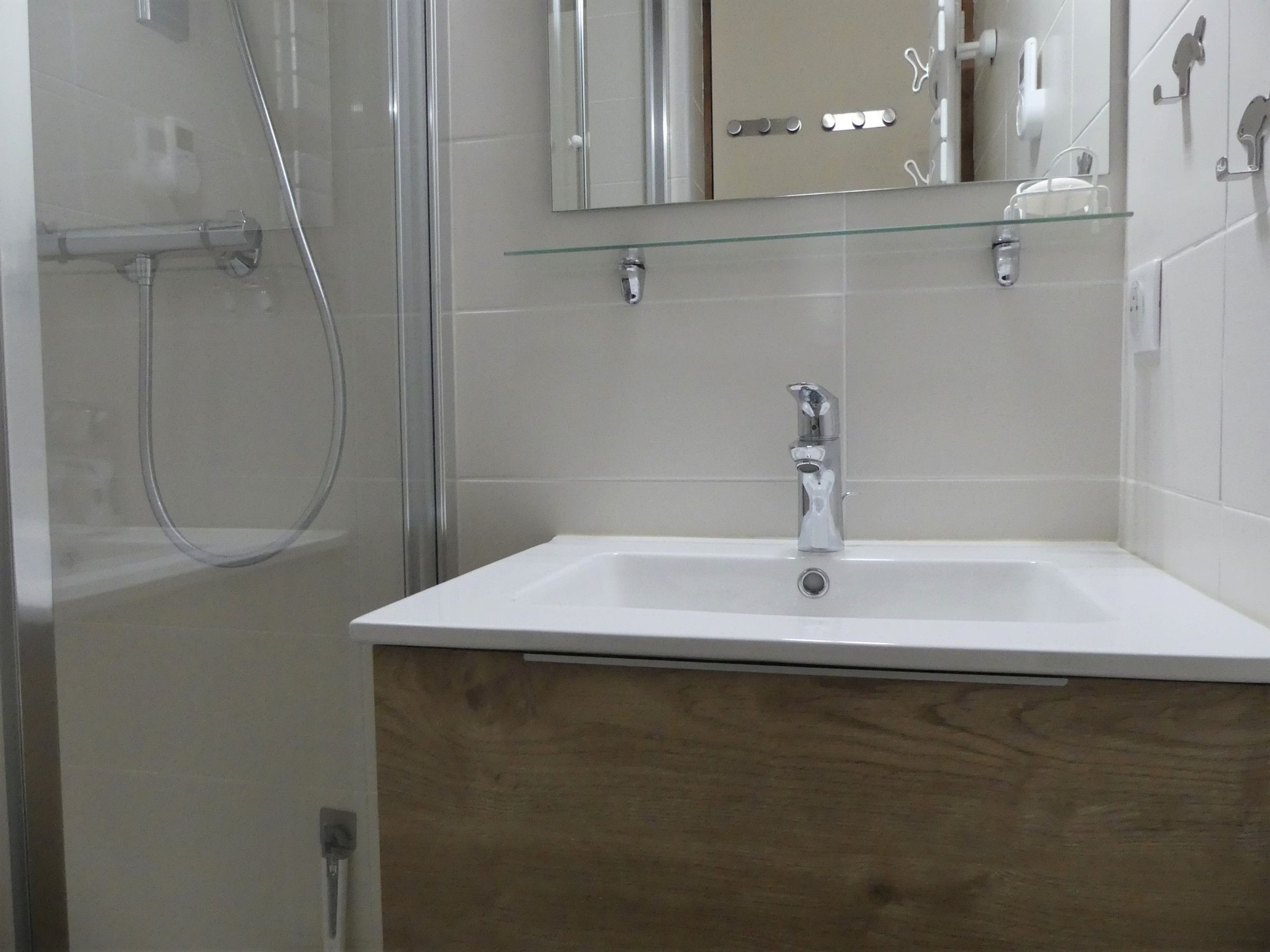 A bathroom with a glass shower enclosure, a white sink, and a wooden vanity.