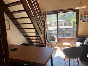 Ein Zimmer mit einer Holztreppe, einem Esstisch, einer Couch und Blick auf ein Haus durch ein großes Fenster.