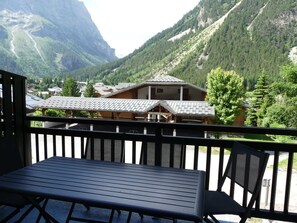 A balcony with a table and chairs overlooking a mountainous landscape with buildings. - Cozy mezzanine studio - 4 guests (Pralognan-la-Vanoise)