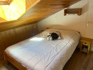 Ein Schlafzimmer mit Holzboden, einem Bett mit weißer Bettwäsche, einem Kissen mit Kuhmuster und einem kleinen Nachttisch mit herzförmiger Dekoration.