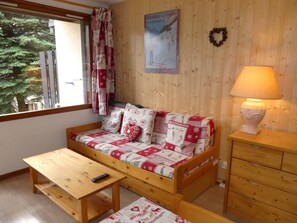 Ein gemütliches Zimmer mit einer Holzsofa, einem kleinen Tisch, einer Lampe und einem Poster an der Wand.