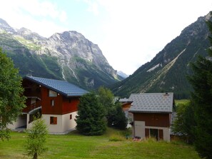 Eine Bergingerhütte mit Satteldach, umgeben von üppiger Vegetation und Bergen.