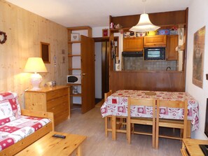 Um quarto acolhedor com uma cama de madeira, uma mesa de jantar com cadeiras, uma cozinha com armários e micro-ondas, e uma luminária em uma mesa de cabeceira.