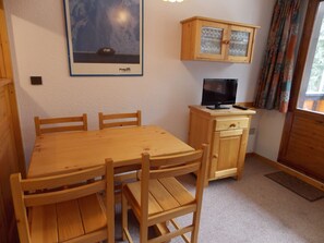 A wooden dining table with chairs, a television on a wooden cabinet, and a framed picture on the wall. - Studio-cabin with WIFI - 4 guests (Pralognan-la-Vanoise)