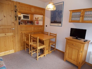 Ein Holzinterieur mit einem Esstisch, Stühlen, einem Fernseher auf einer Holzkommode und einer Wandleuchte.
