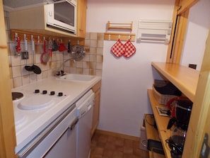 A compact kitchen with a sink, stove, and microwave. There are hanging utensils and a small shelf with a coffee maker. - Studio-cabin with WIFI - 4 guests (Pralognan-la-Vanoise)