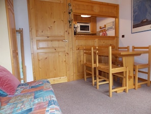 A bedroom with a bed, a wooden door, a small kitchenette, and a dining area with chairs and a table. - Studio-cabin with WIFI - 4 guests (Pralognan-la-Vanoise)