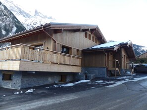 Eine Holzhütte mit Steinfundament, Holzbalkon und einem geparkten Auto davor.