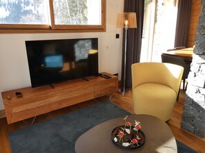 Un soggiorno moderno con una TV a schermo piatto, un mobile TV in legno, una poltrona gialla e una parete in pietra.