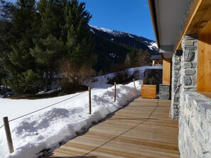 Eine Holzterrasse führt zu einem Steinhaus mit Blick auf einen Berg.