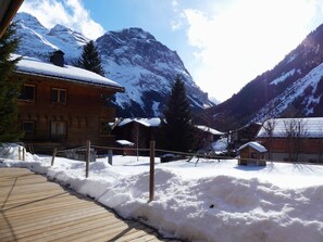 Une cabane en bois, dont le toit est recouvert de neige, entourée de montagnes enneigées et dotée d’une terrasse en bois.