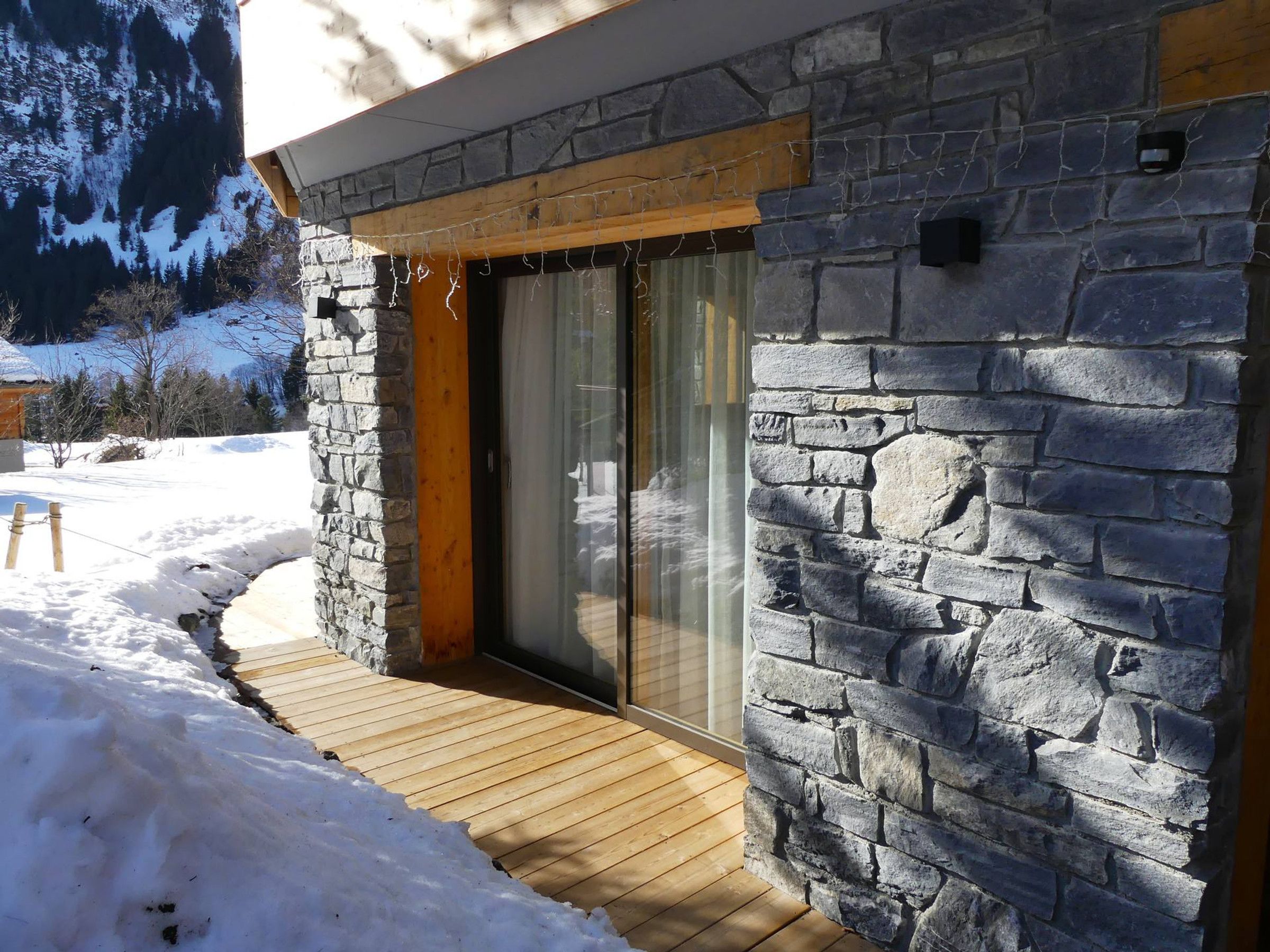 Un bâtiment en pierre doté d’une terrasse en bois et d’une porte en verre.