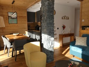 A cozy interior with a dining area, a stone pillar, a living room with a blue sofa, and a kitchen in the background. - Apartment with mountain views - 4 guests (Pralognan-la-Vanoise)