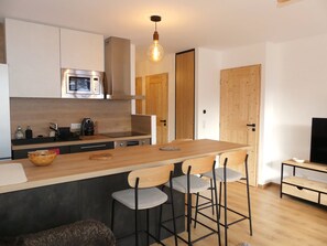 A modern kitchen with a central island, bar stools, a microwave, and a wooden door. - Ideal apartment near slopes - 4 guests (Pralognan-la-Vanoise)