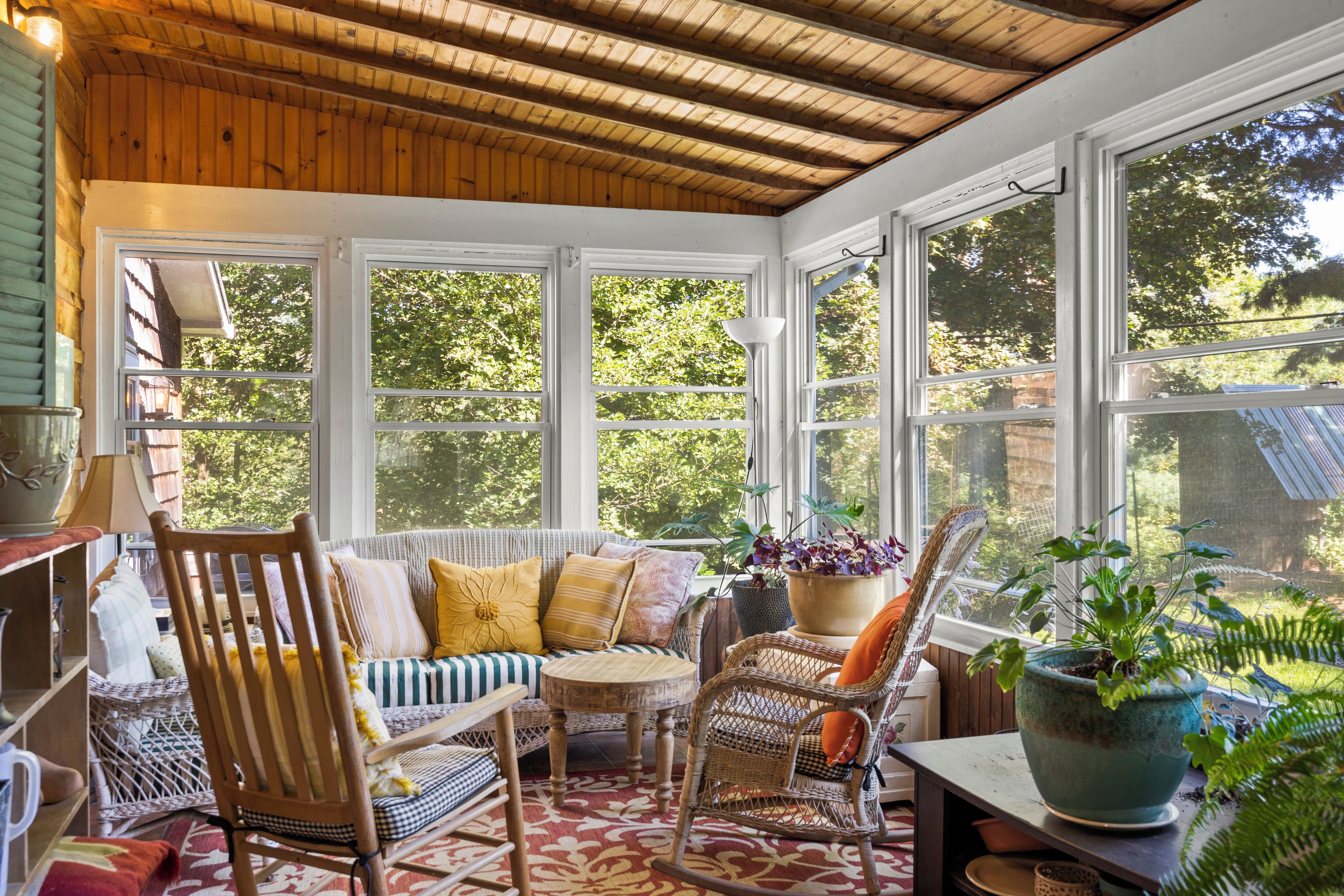A sunroom with a wooden ceiling, large windows, and a seating area with chairs and a sofa.