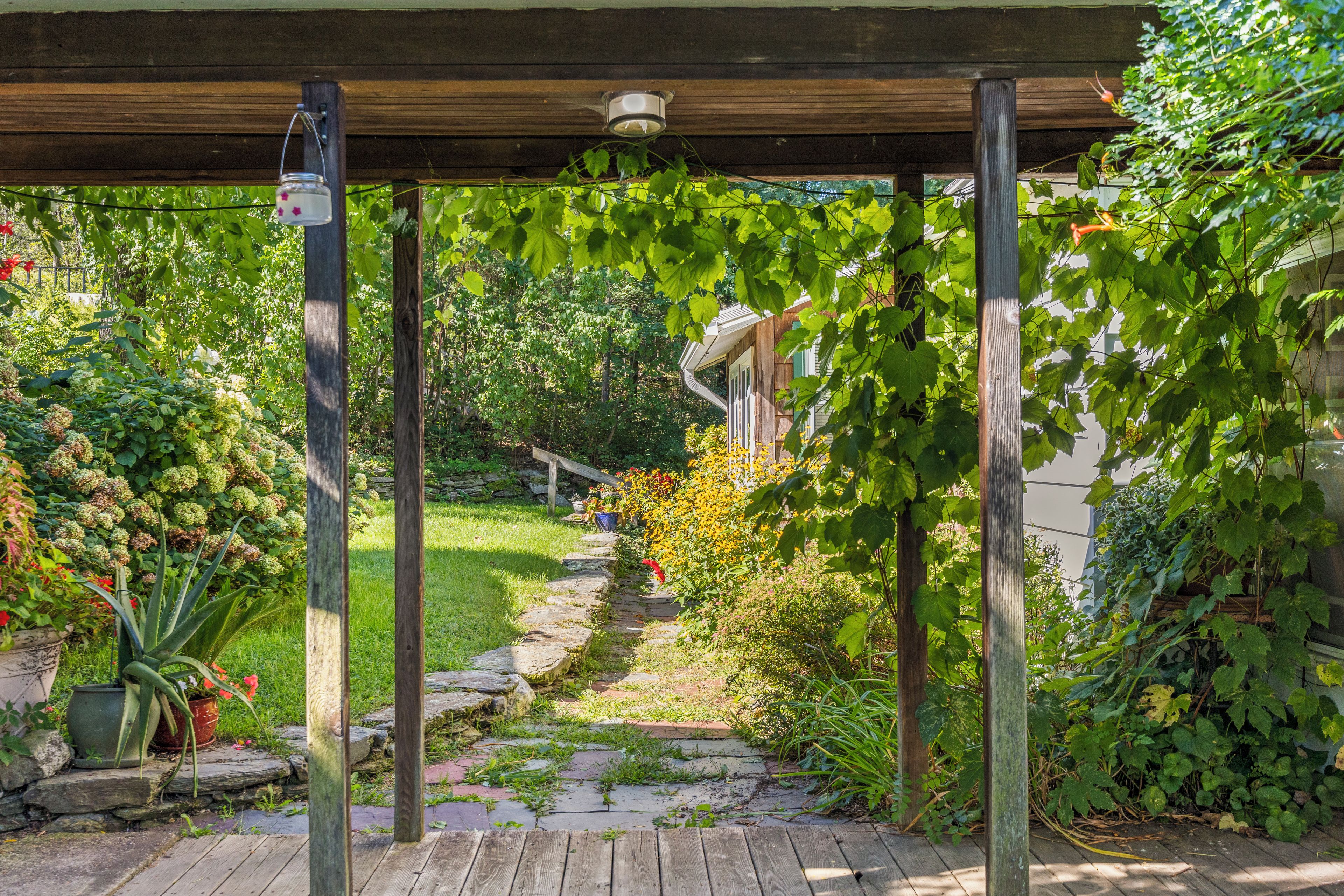 A wooden pergola structure with a stone pathway leading through a garden.