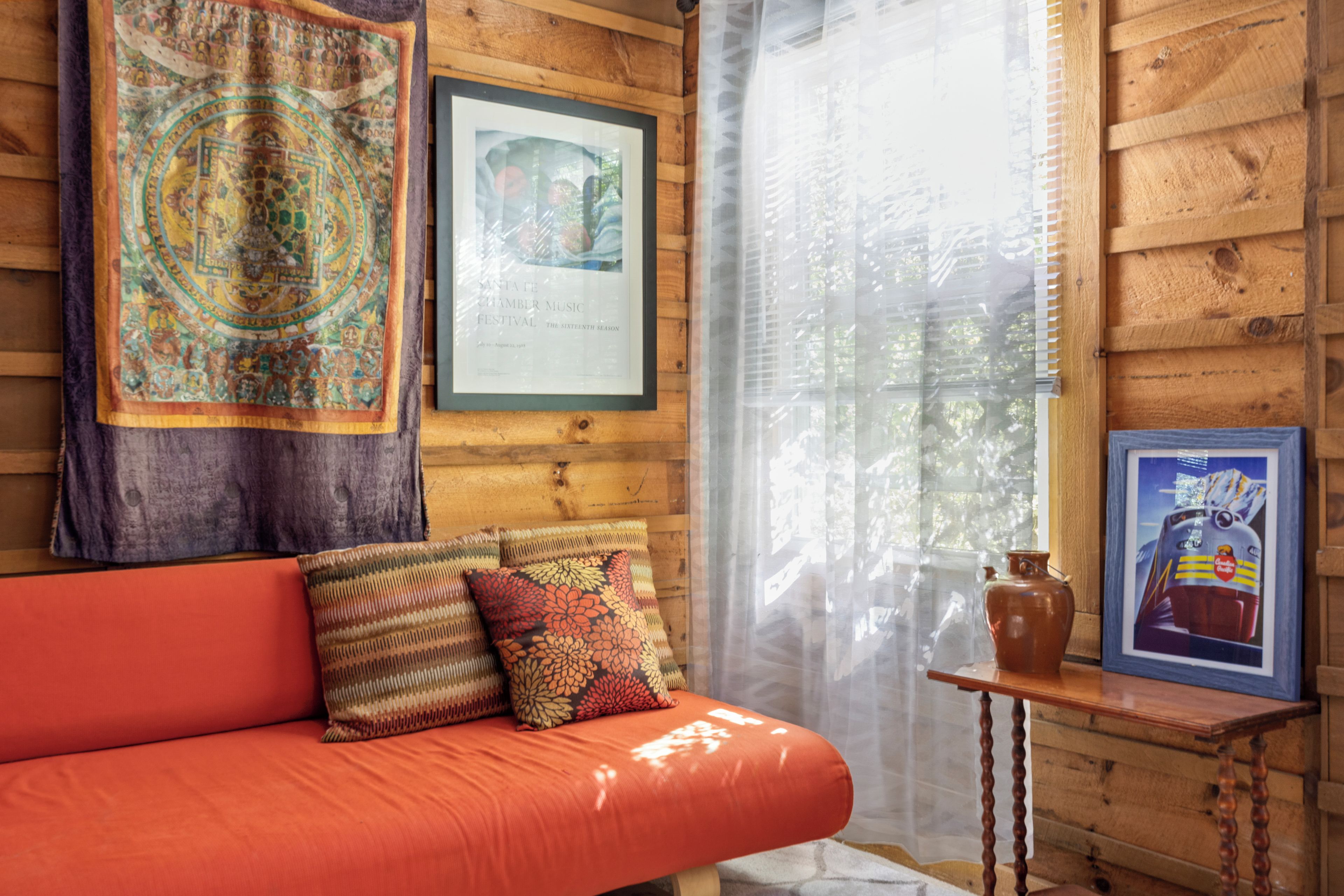 A wooden cabin interior with a red sofa, patterned cushions, a framed certificate, and a small table with a vase.