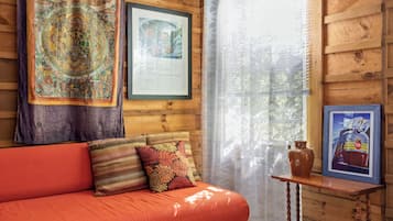 A wooden cabin interior with a red sofa, patterned cushions, a framed certificate, and a small table with a vase.