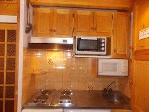 Une cuisine de taille réduite, dotée de meubles en bois, d’une cuisinière, d’un évier et de deux fours à micro-ondes.