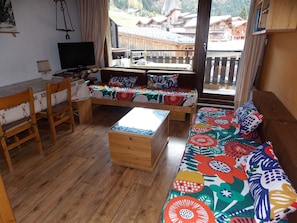 Une pièce avec un plancher en bois, un canapé recouvert d’un tissu à motifs floraux colorés, une table basse en bois et un téléviseur posé sur un meuble.